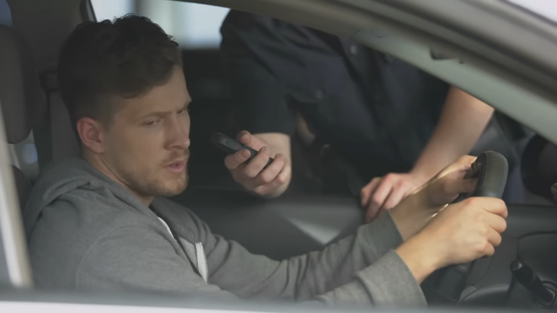 A Driver Looks Frustrated as A Police Officer Offers a Breathalyzer Test During a Traffic Stop