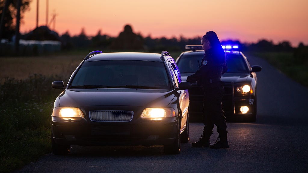 Police officer conducting a DUI traffic stop with patrol car lights at sunset