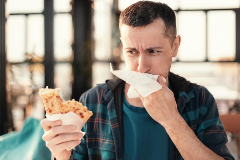 Man feeling nauseous while eating pizza, possible food poisoning after restaurant meal