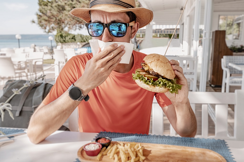 Man feeling nauseous while eating a burger at a restaurant, possible food poisoning symptoms after a meal