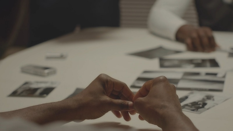 Close-up of a person's hands folded on a table during a police interrogation, without handcuffs visible