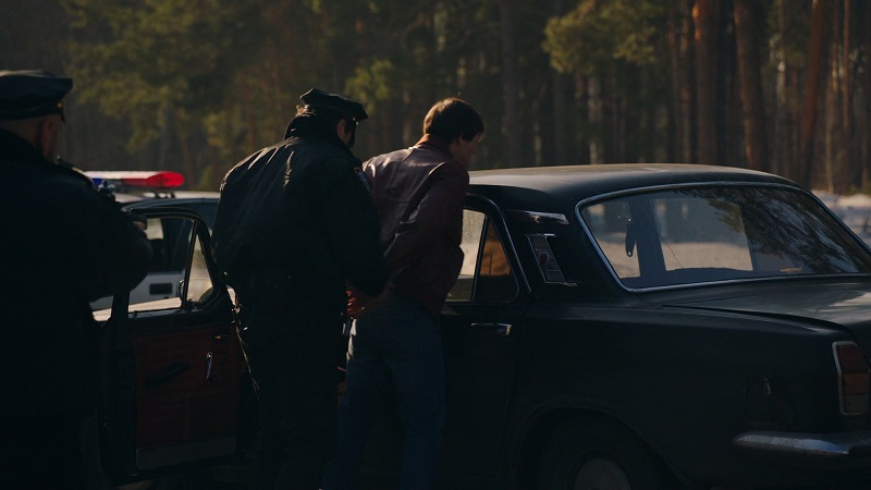 Police officers arrest a person next to a car in a wooded area, detaining them without clarifying their rights