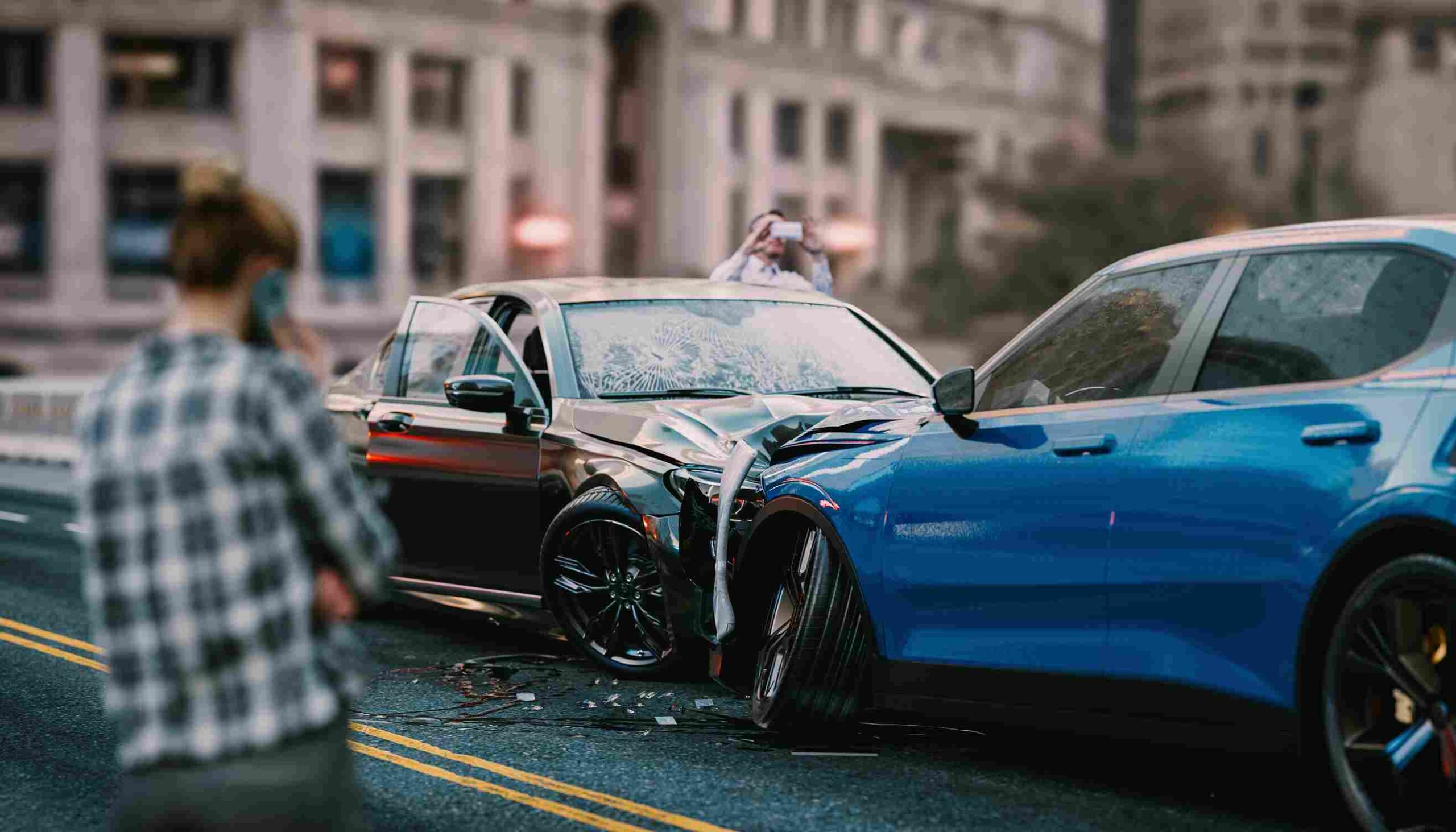 Two heavily damaged cars after a collision on a city street while a person photographs the accident scene