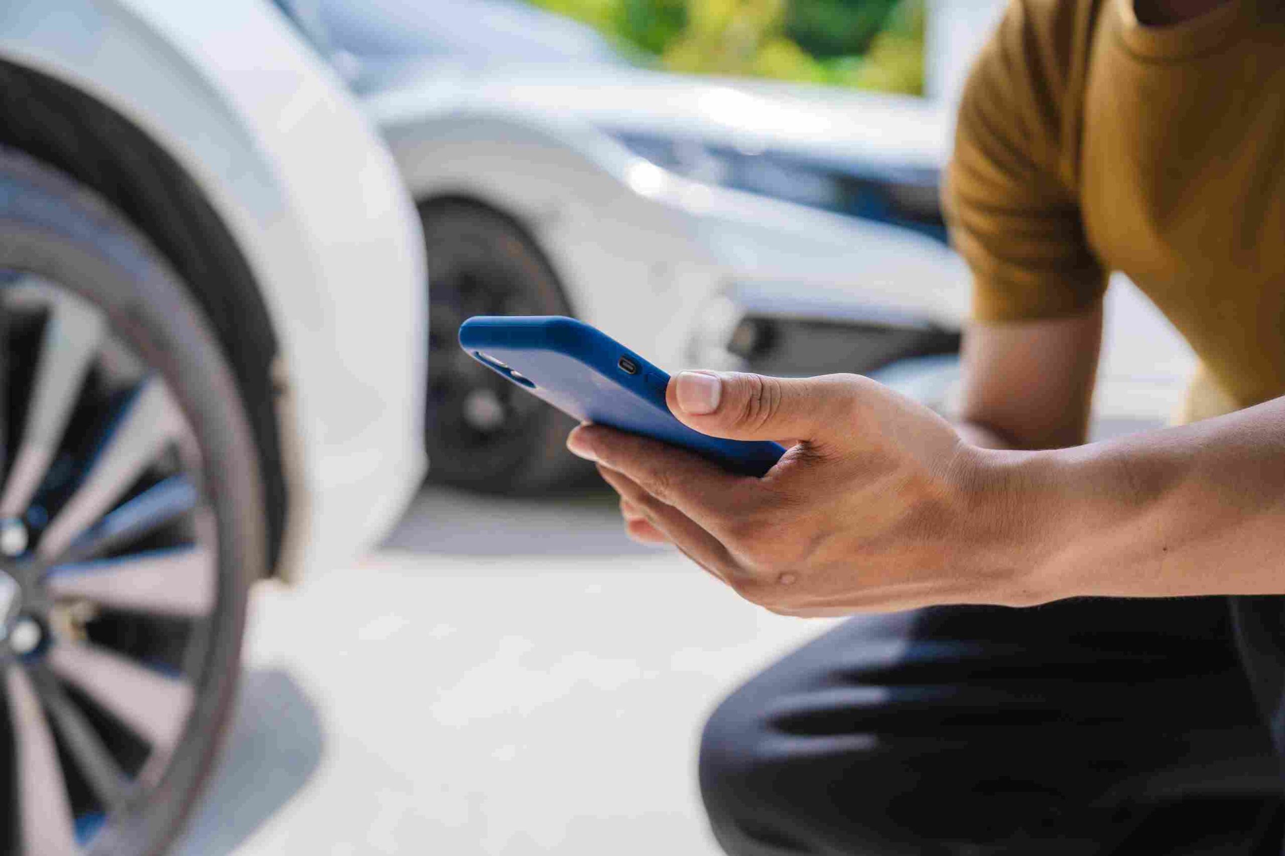 A person holding a smartphone near parked cars while reporting a car accident