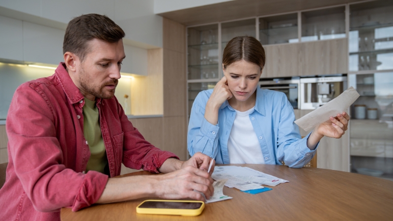 Couple reviewing bills and paperwork at a table while discussing debt and financial obligations