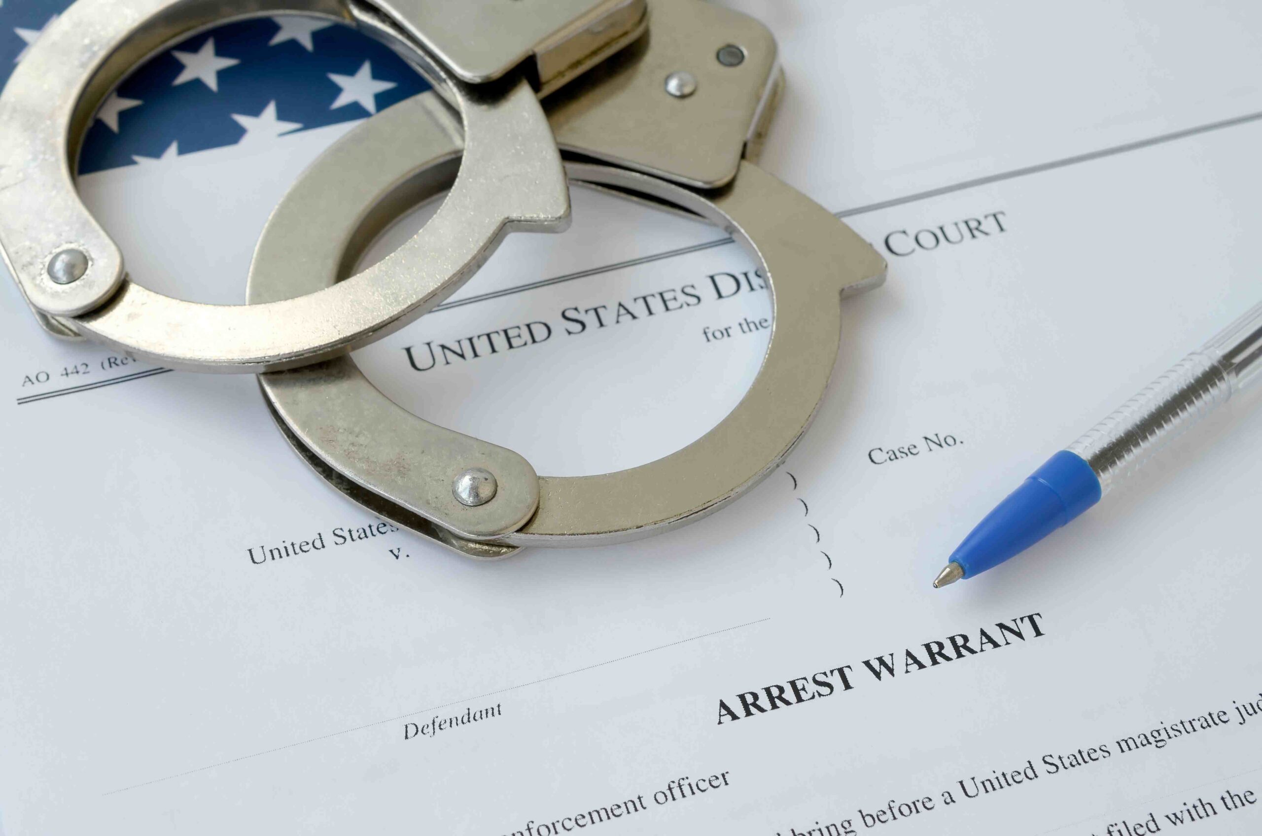 Handcuffs placed on a legal document labeled arrest warrant with a pen nearby