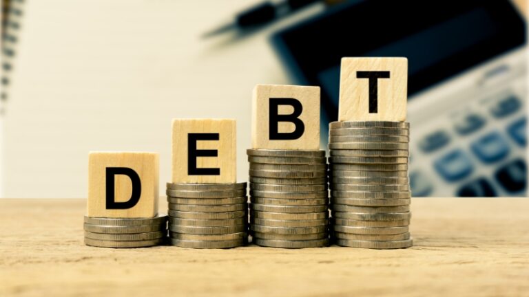 Stacks of coins with wooden blocks spelling “debt” placed in front of a calculator representing personal debt