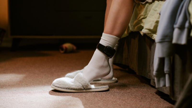 Person wearing an electronic ankle monitor while sitting at home during parole supervision