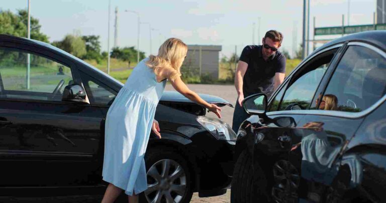Two drivers standing near their damaged cars after a collision while discussing the accident