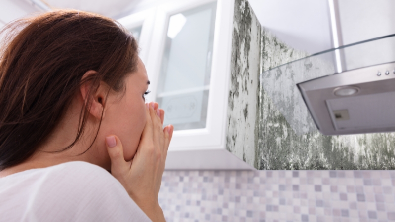 Tenant covering her mouth while looking at heavy mold growth on a kitchen wall